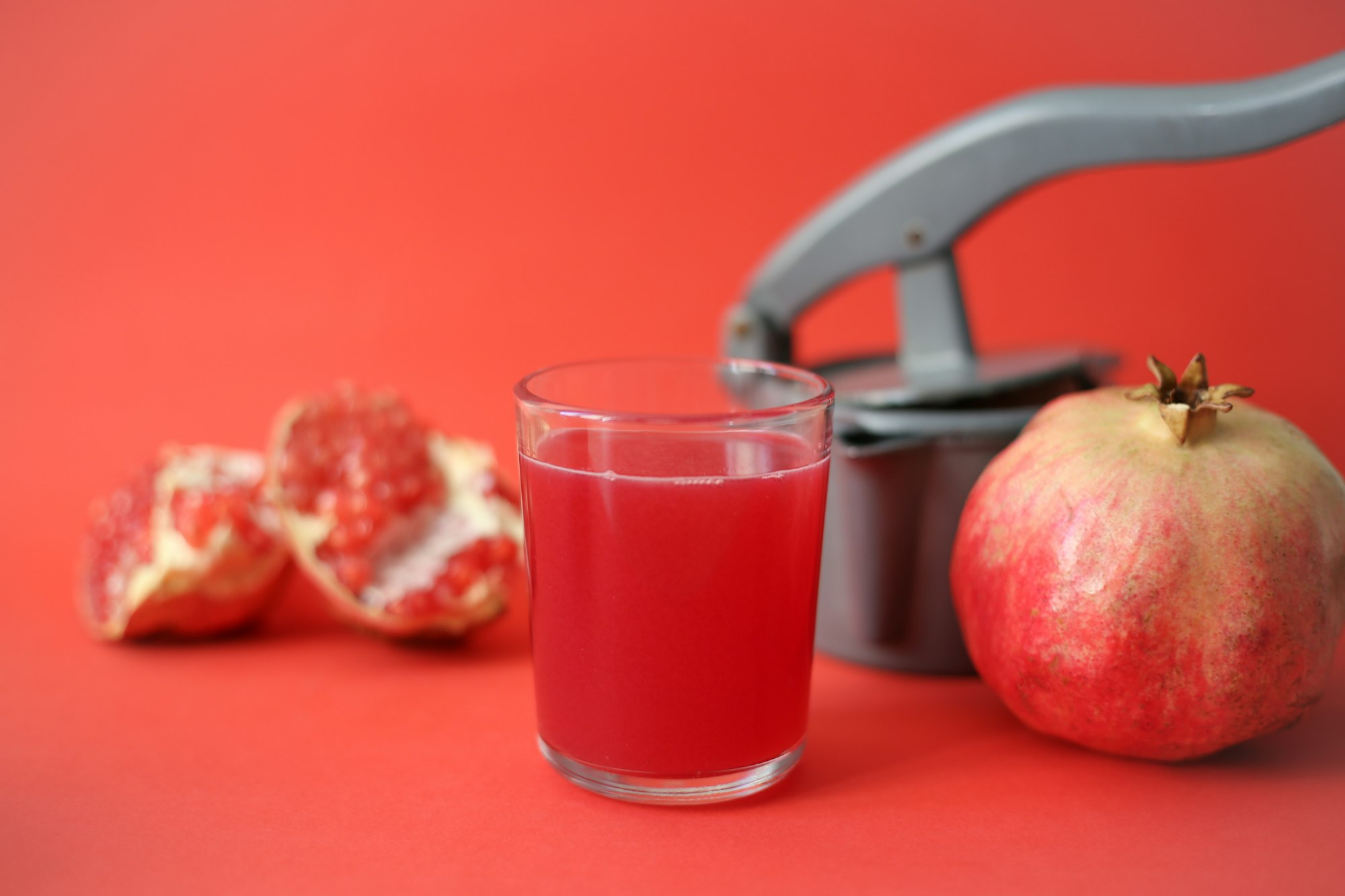 clear drinking glass with red juice beside Pomegranate fruit