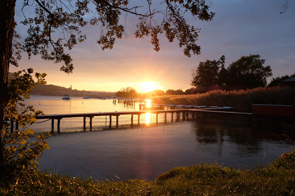 A serene lakeside scene with a wooden dock stretching into calm water under a soft sunset.