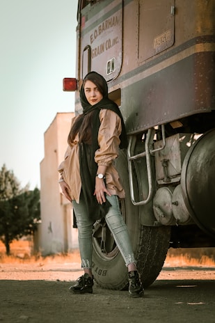 A confident truck driver standing beside a sleek semi-truck under a clear blue sky.