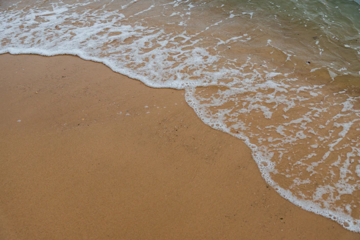 A gentle wave rolling onto a sandy beach, evoking the natural rhythm of breath and relaxation.