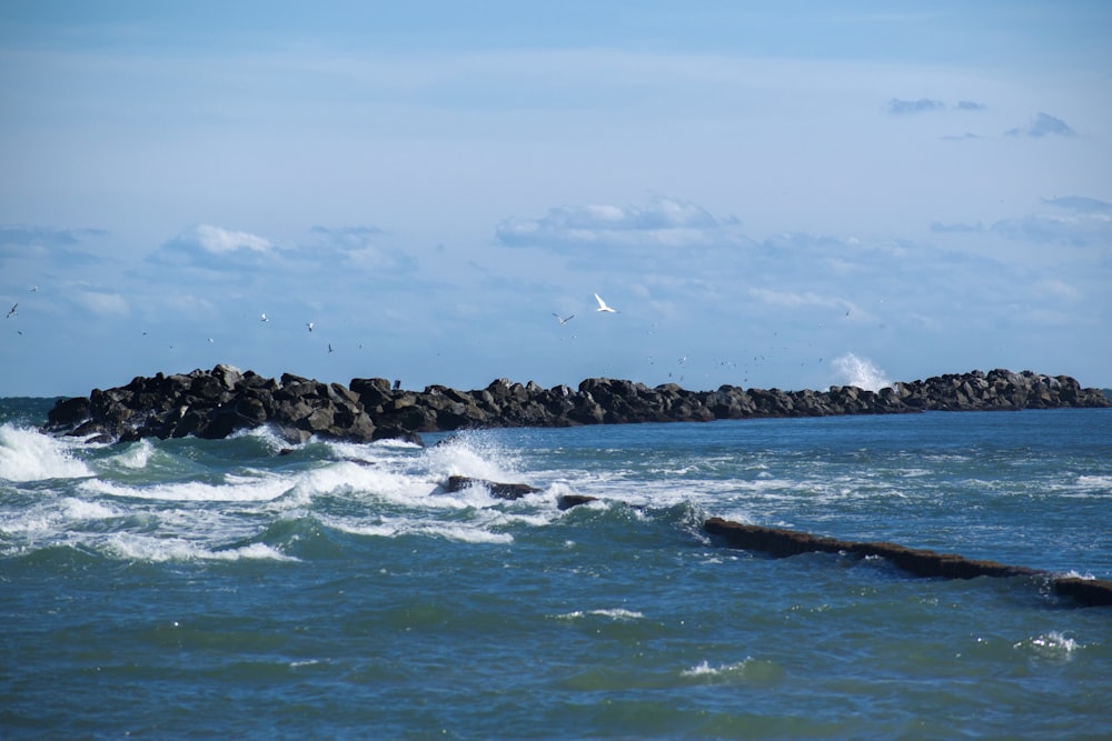 Onde dell'oceano che si infrangono sulle rocce sotto il cielo blu durante il giorno