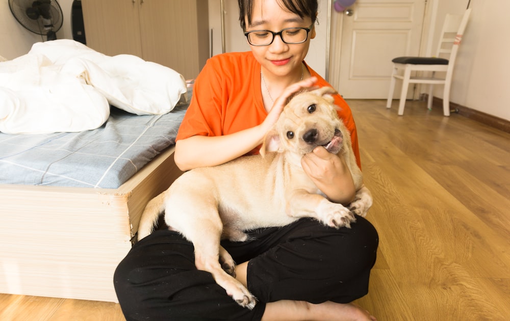 woman in orange shirt hugging white short coated dog