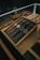 A collection of five wristwatches neatly arranged on a gray felt-lined wooden tray within a glass display case. The watches have various designs and styles, with brown and black leather straps. The lighting creates a warm and elegant ambiance, highlighting the watches and their details.