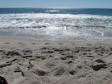 Morning beach scene with soft waves and footprints in the sand near Oceanis guesthouse.