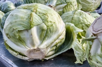 Heads of green cabbage stacked in a market setting, ready for bulk supply.