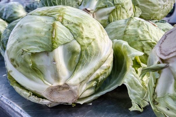 Heads of green cabbage stacked in a market setting, ready for bulk supply.