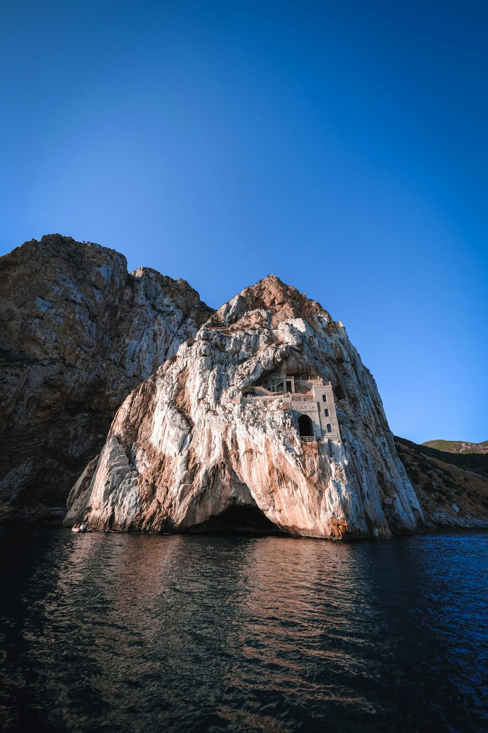 brown rock formation on body of water under blue sky during daytime