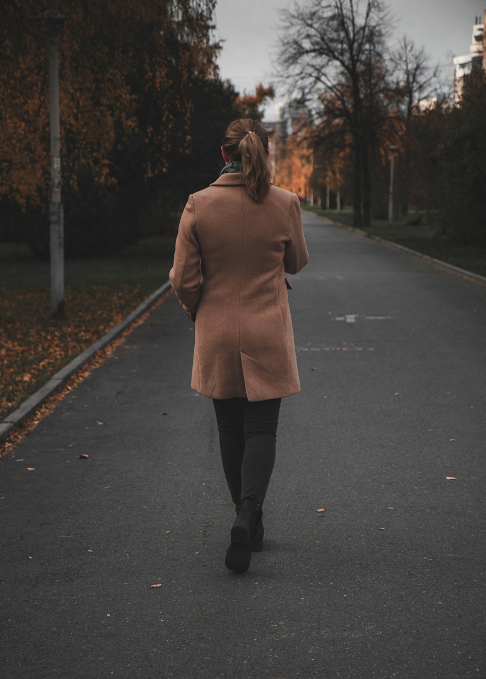 woman in brown coat standing on road during daytime