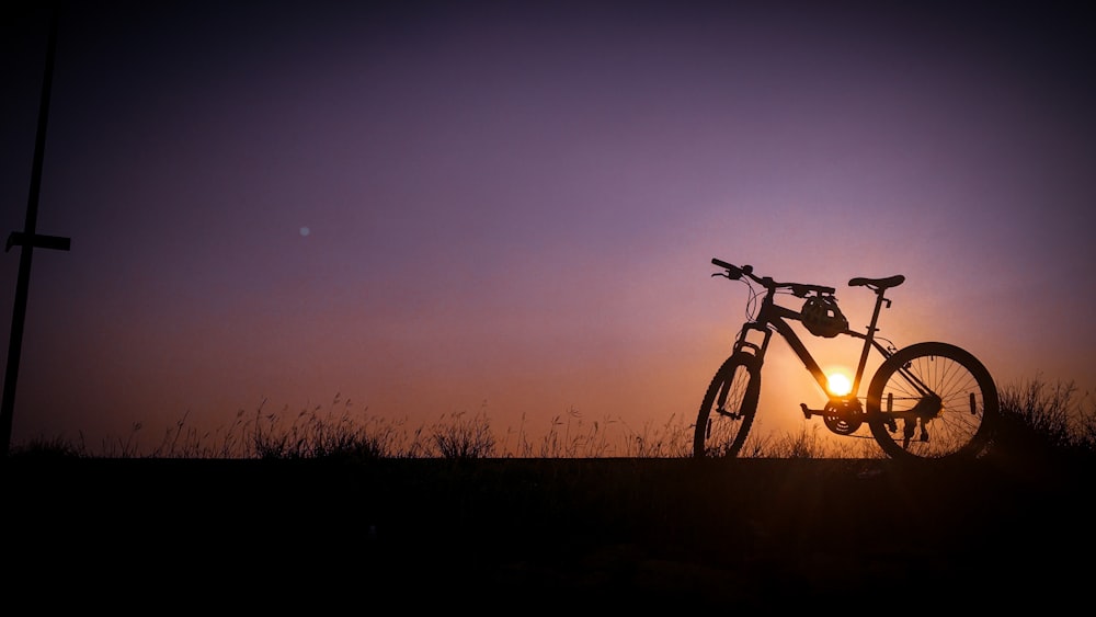 silhouette of bicycle on grass field during sunset