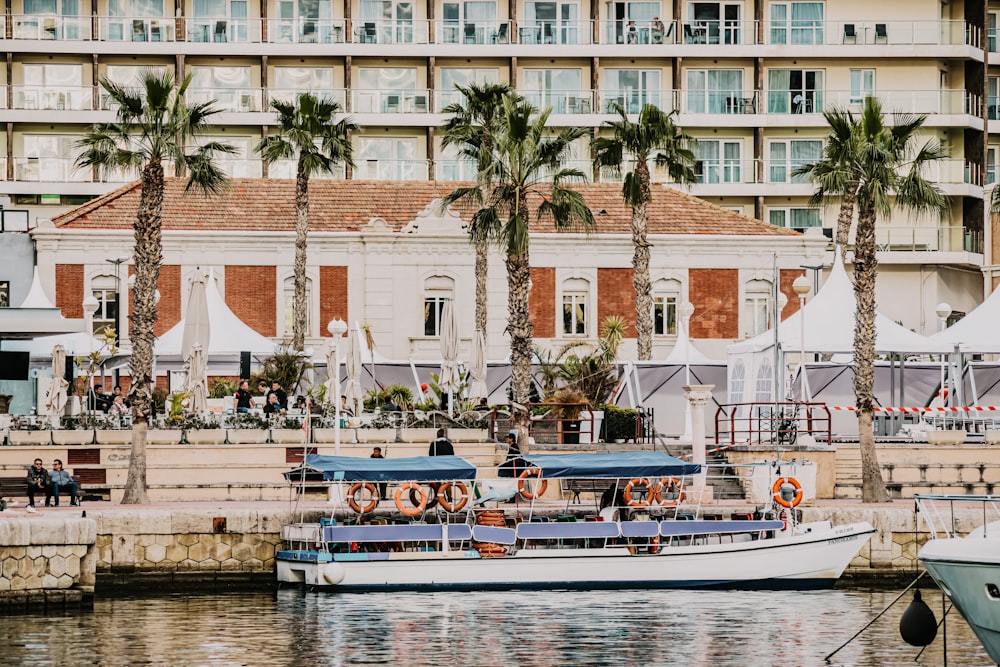 white and blue boat on body of water near white concrete building during daytime