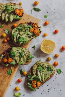Fresh avocado toast topped with cherry tomatoes and microgreens on wooden board.