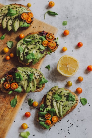 Fresh avocado toast topped with cherry tomatoes and microgreens on wooden board.