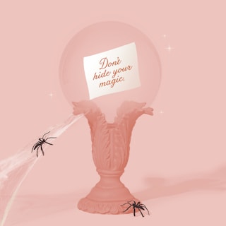 A decorative pedestal with an ornate design holds a transparent sphere featuring a message that reads 'Don't hide your magic.' Two black spiders and cobwebs add an eerie touch to the pastel pink setup.