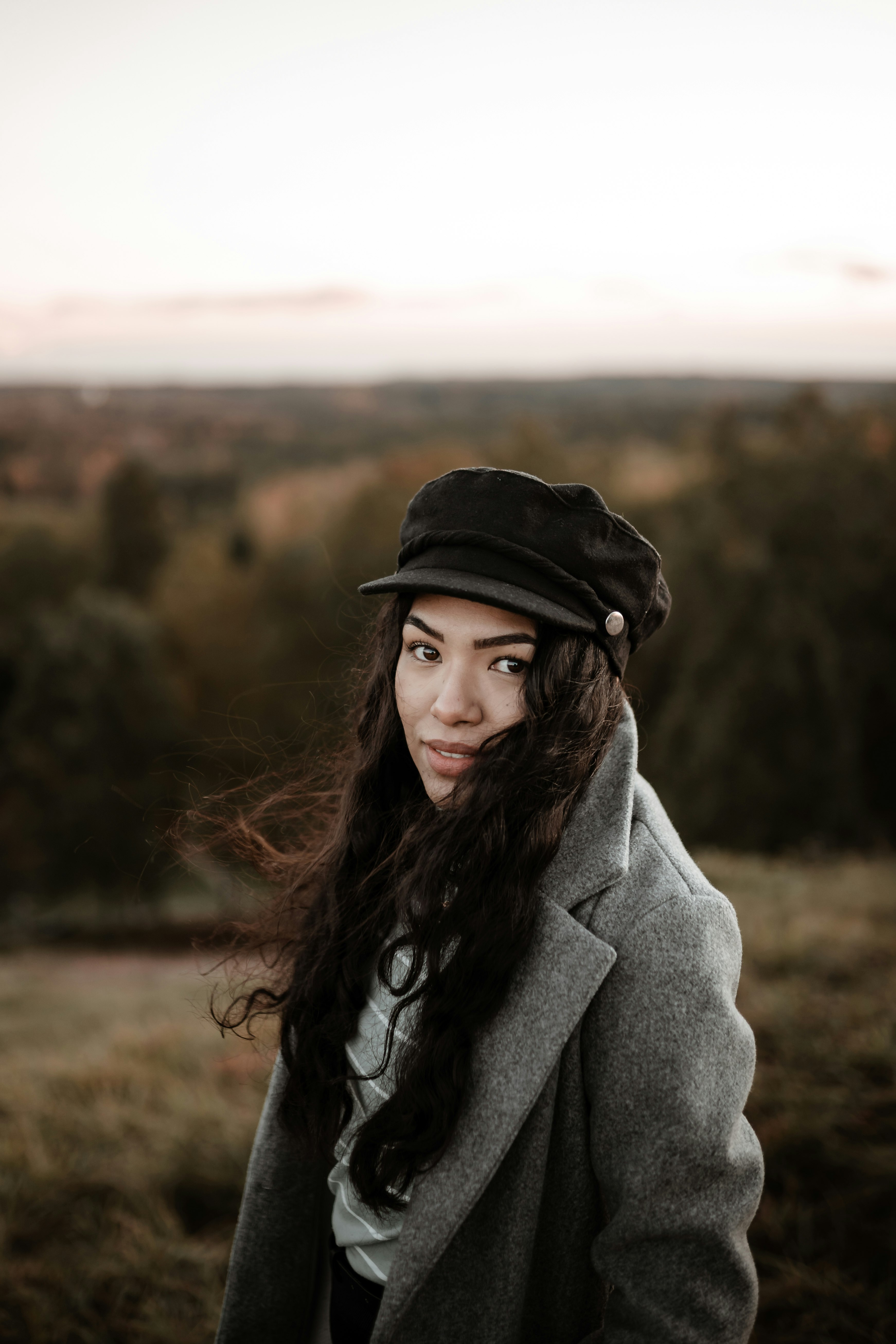 woman in gray coat and black hat standing on brown field during daytime