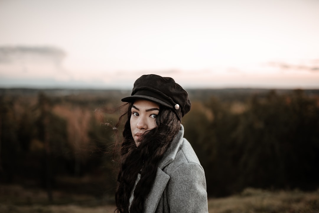 woman in gray coat and black hat standing on brown field during daytime