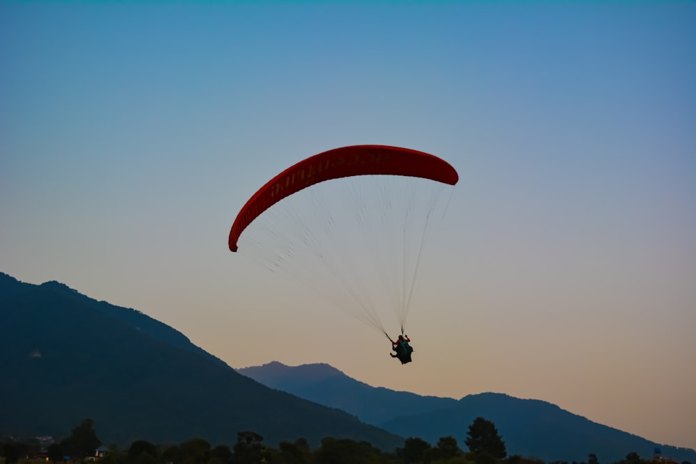 person in red parachute over mountains during daytime