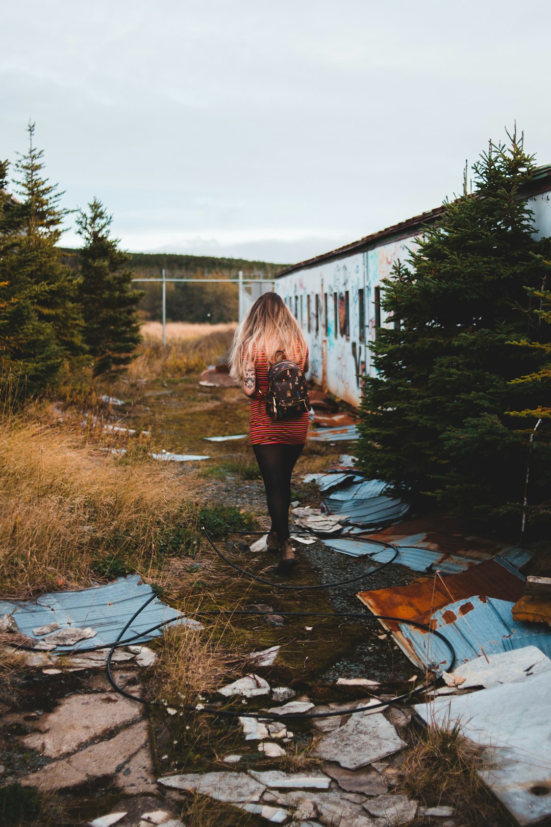 woman in red jacket standing on brown soil near green trees during daytime