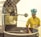 A person wearing a yellow uniform and a blue chef's hat is operating a large industrial machine used for roasting coffee beans. The person is inspecting a batch of beans inside a circular roasting drum. The machine is metallic and has the brand 'JOPER' displayed prominently on it.