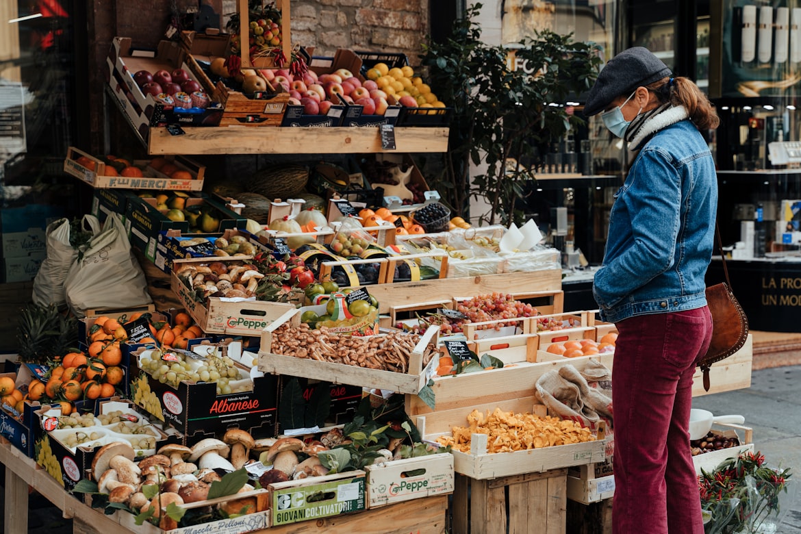 Person in denim jacket standing in front of a fruit stand