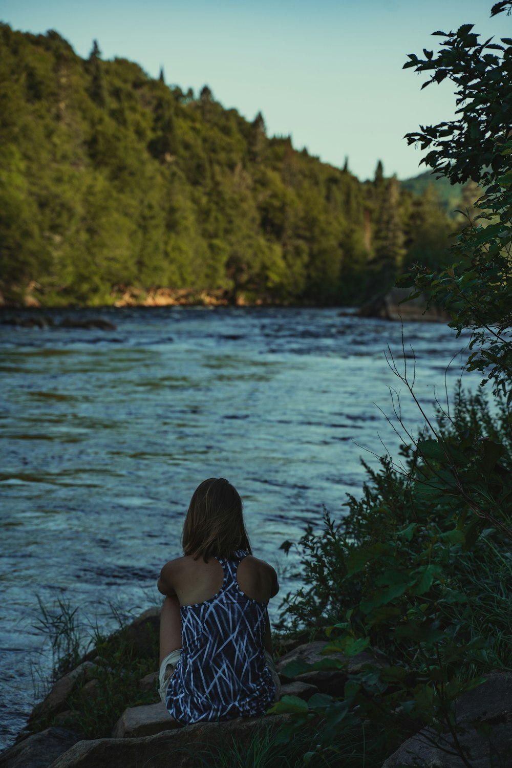 girl in blue and white polka dot dress sitting on green grass near body of water