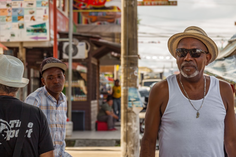 man in white tank top wearing brown hat standing near store during daytime