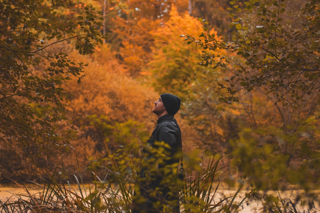 man in black jacket standing near brown trees during daytime