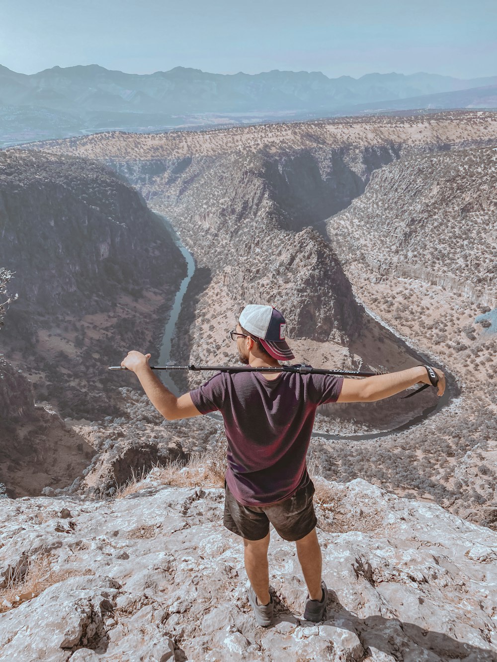 man in grey t-shirt and black shorts holding black stick standing on rocky hill during