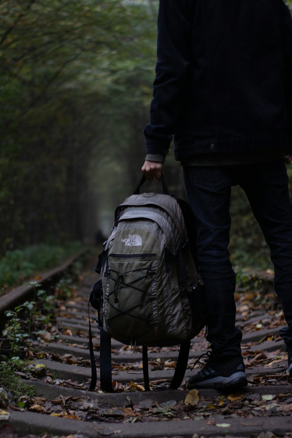 person in black jacket and black pants carrying gray backpack walking on pathway