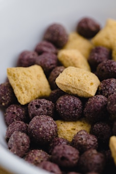 A close-up view of a mix of cereal pieces, including light brown pillow-shaped pieces and dark purple spherical puffs.