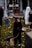 Several Halloween decorations are set up on a lawn, including witch figurines wearing dark robes and pointy hats, holding broomsticks, along with other spooky figures like a ghost figure in the background. The scene is set in front of a house, with other yard decorations visible.