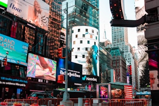 A bustling urban scene features a myriad of colorful advertisements on buildings in a lively city setting. Skyscrapers adorned with bright digital billboards display various advertisements and branding. Traffic signals and vehicles are present in the foreground, with people visible around the area.