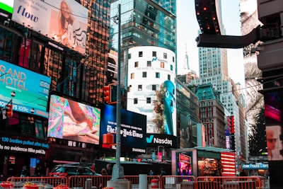 A bustling urban scene features a myriad of colorful advertisements on buildings in a lively city setting. Skyscrapers adorned with bright digital billboards display various advertisements and branding. Traffic signals and vehicles are present in the foreground, with people visible around the area.