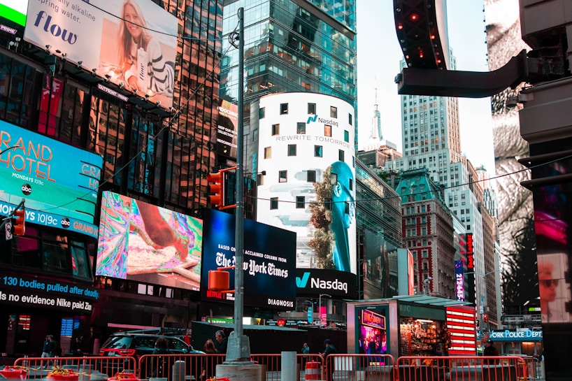 A bustling urban scene features a myriad of colorful advertisements on buildings in a lively city setting. Skyscrapers adorned with bright digital billboards display various advertisements and branding. Traffic signals and vehicles are present in the foreground, with people visible around the area.