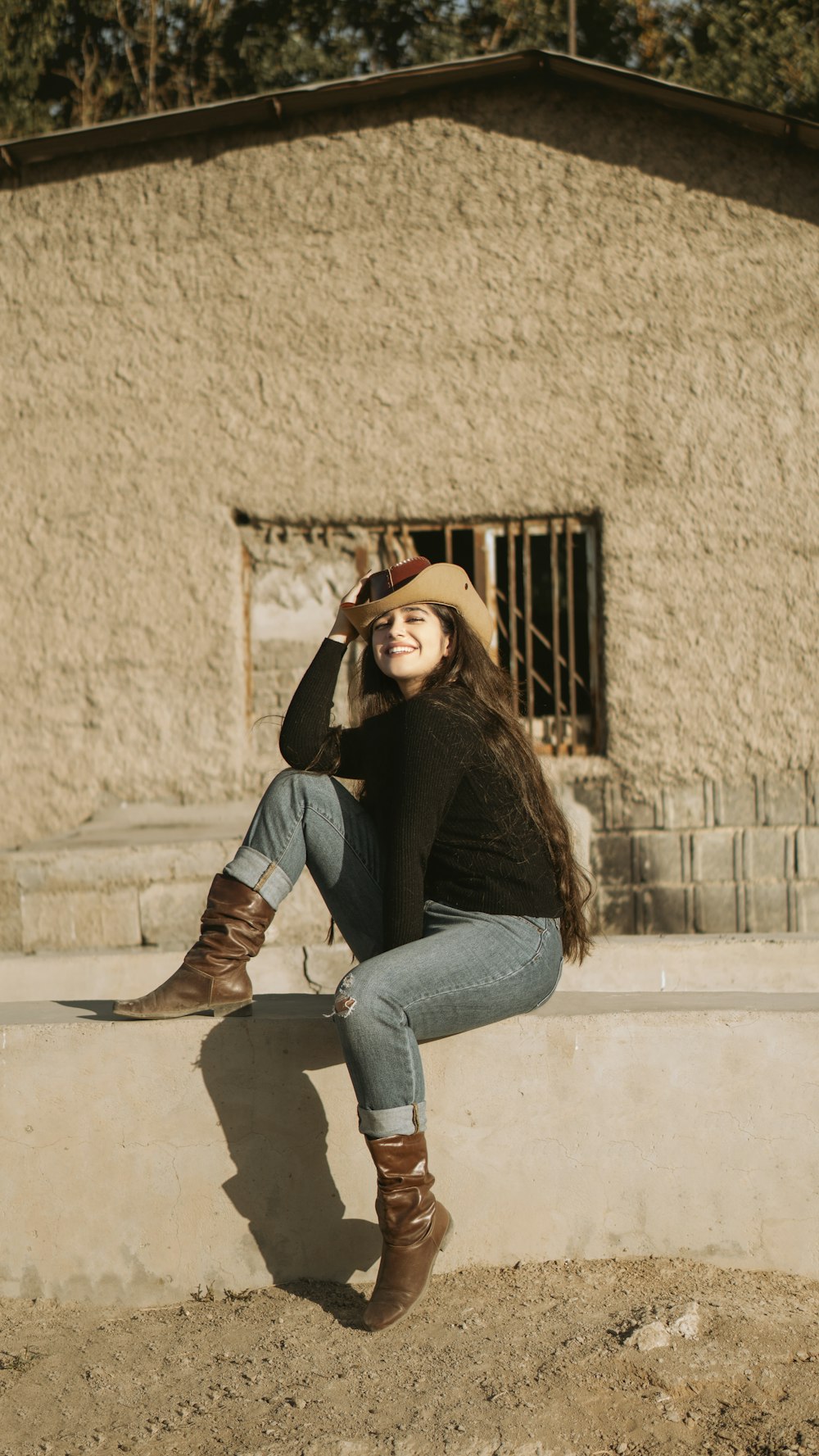 Femme au chapeau marron et chemise à manches longues noire et jean en denim bleu assise sur blanc