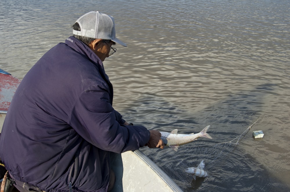 man in black jacket and white cap sitting on white boat during daytime