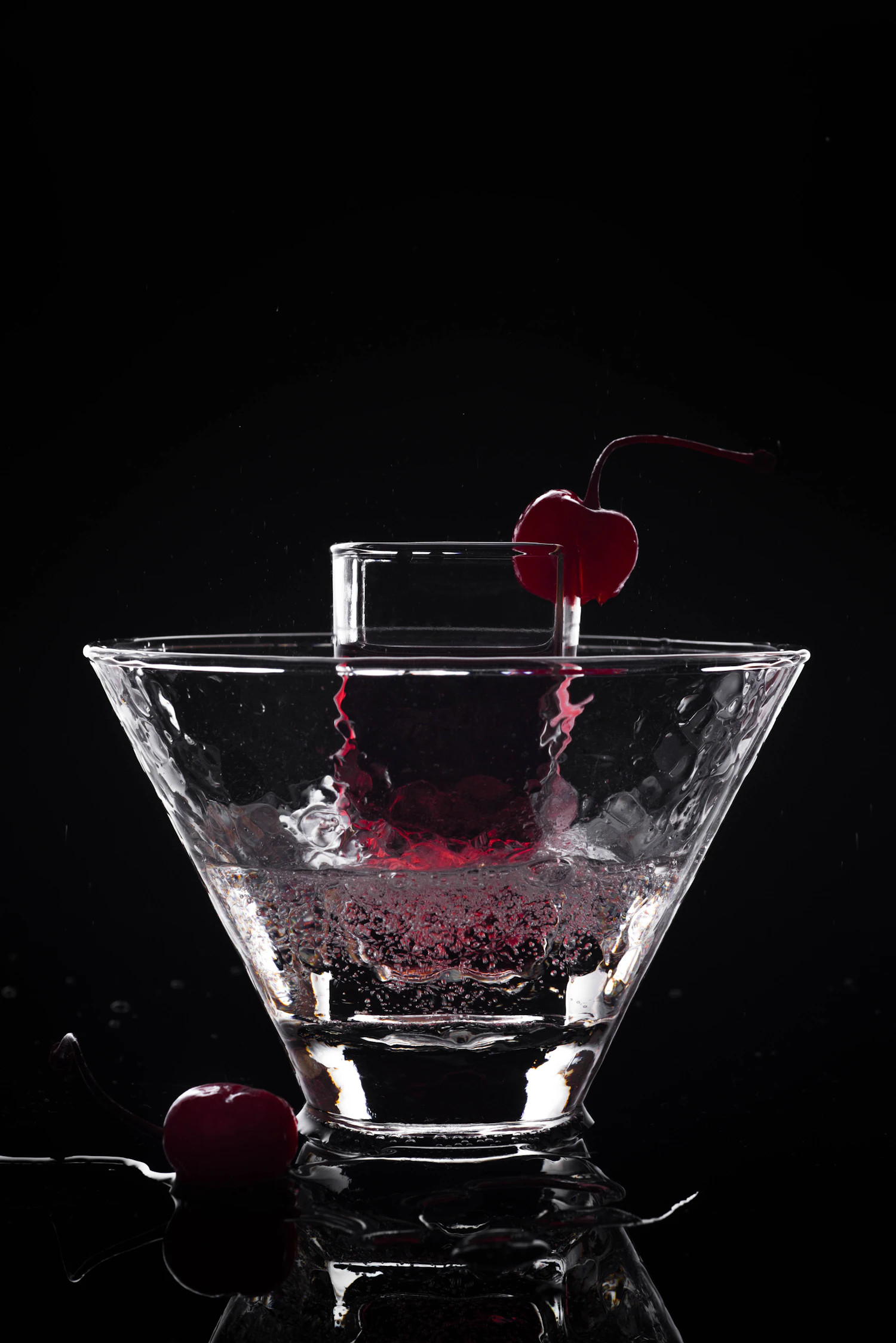 A cherry dropped into a sparkling clear glass of phosphate, splashing on a black ground