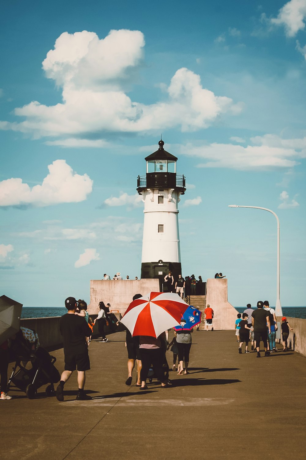 people walking near white and black lighthouse under blue and white cloudy sky during daytime