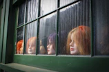 A vibrant red curly wig displayed on a mannequin against a pastel backdrop.