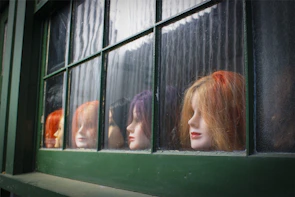 A vibrant red curly wig displayed on a mannequin against a pastel backdrop.