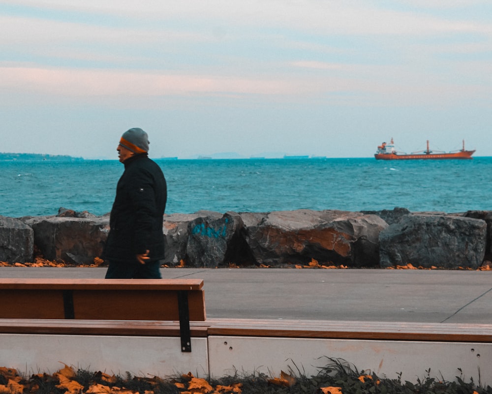 man in black jacket sitting on brown wooden bench looking at the sea during daytime