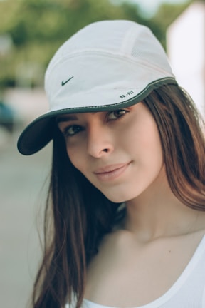 A young person wearing a white cap with a subtle faith-inspired logo, smiling outdoors.