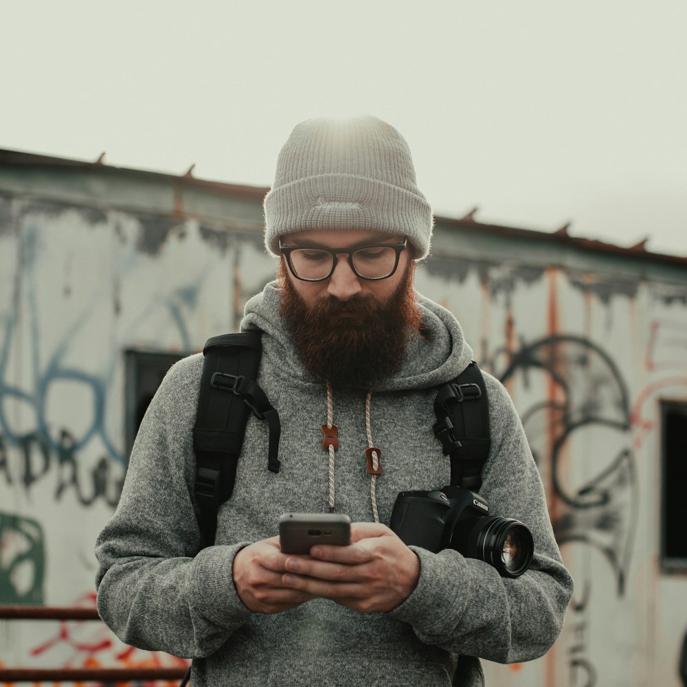 man in gray knit cap and black jacket holding black smartphone