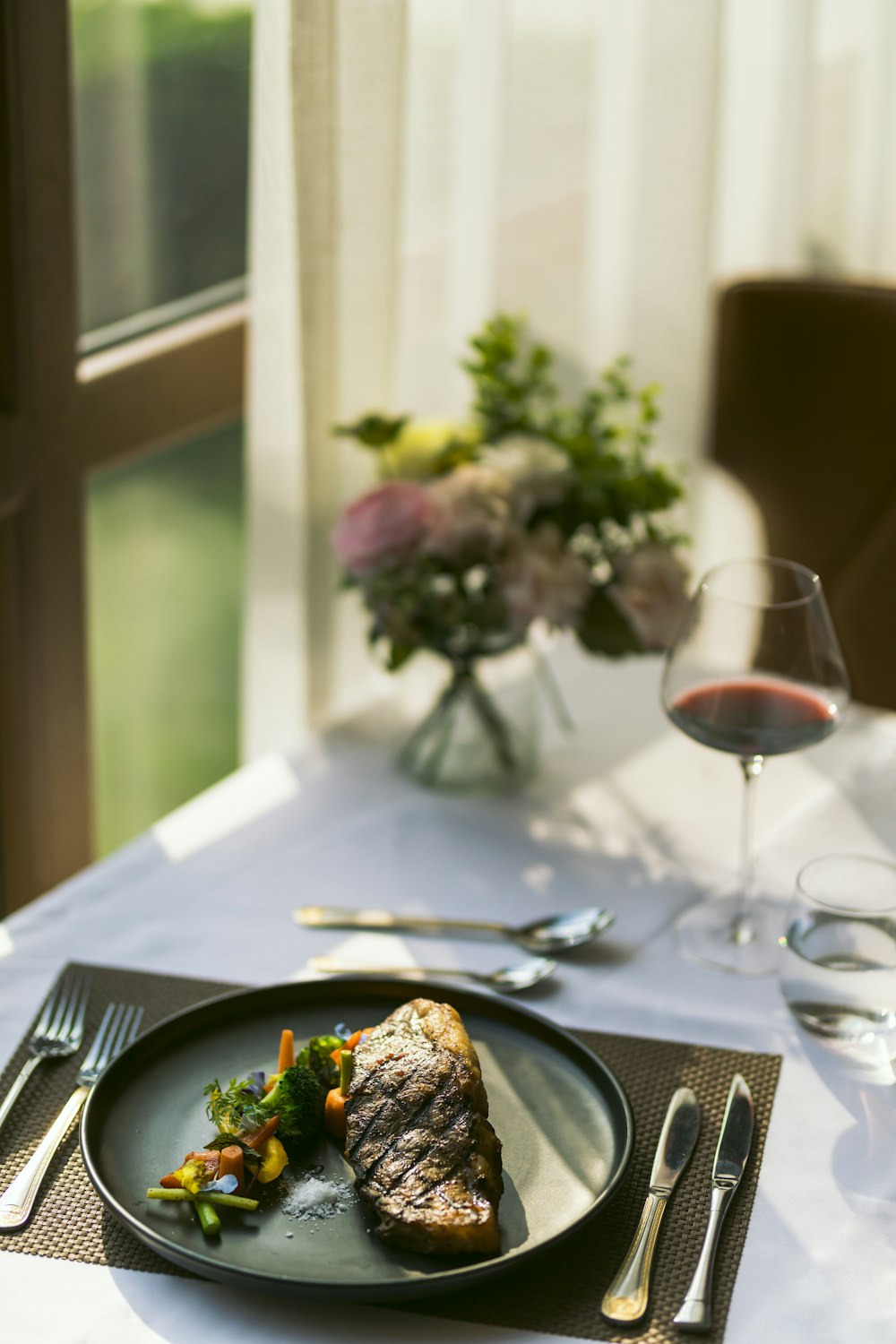 Comida cocinada en un plato de cerámica negra junto a una copa de vino en la mesa