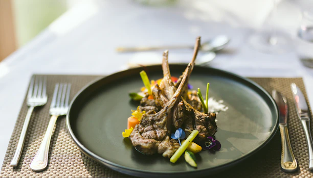 A happy customer enjoying a gourmet lamb dish at a warmly lit dining table.