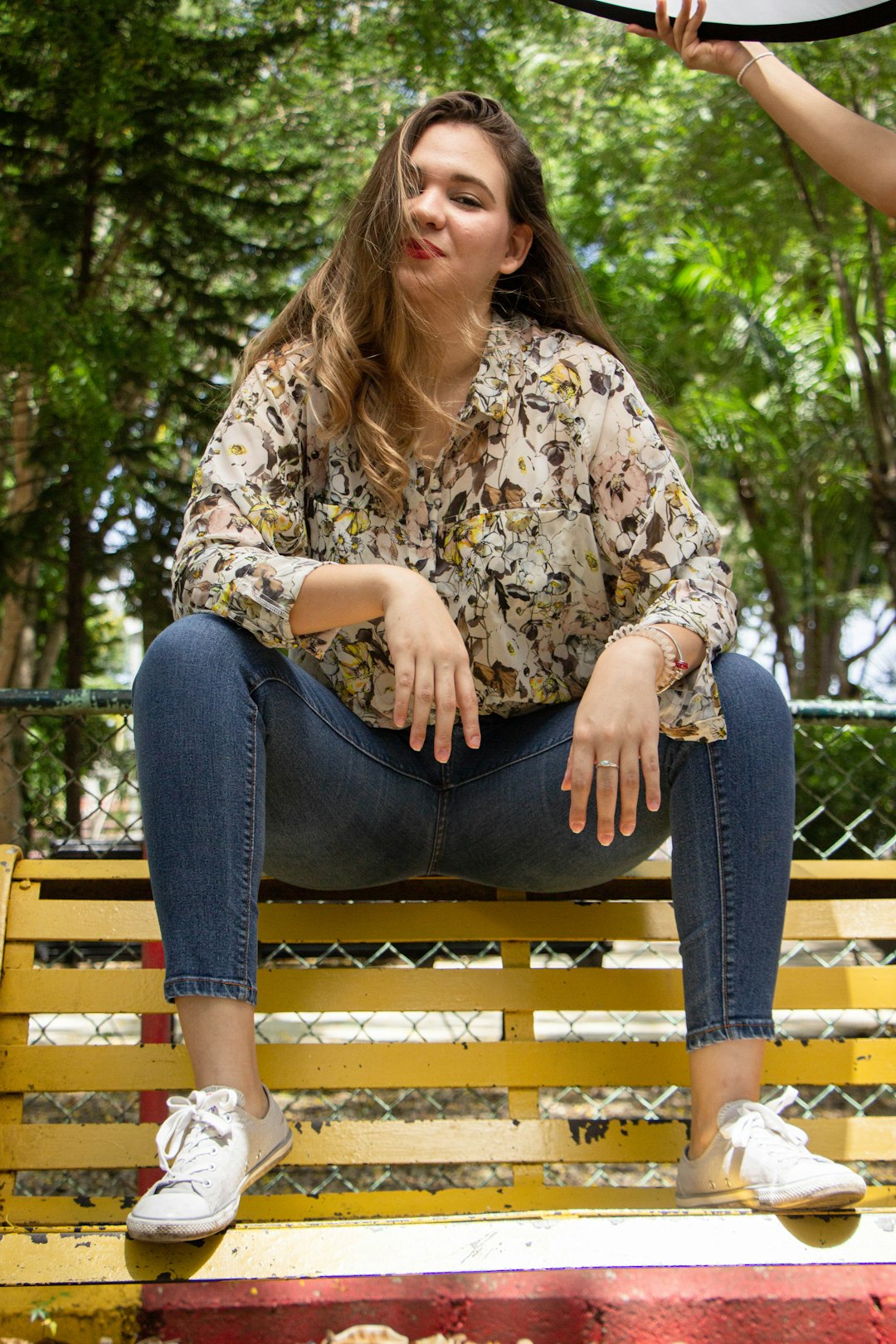 woman in brown and white floral long sleeve shirt and blue denim jeans sitting on brown