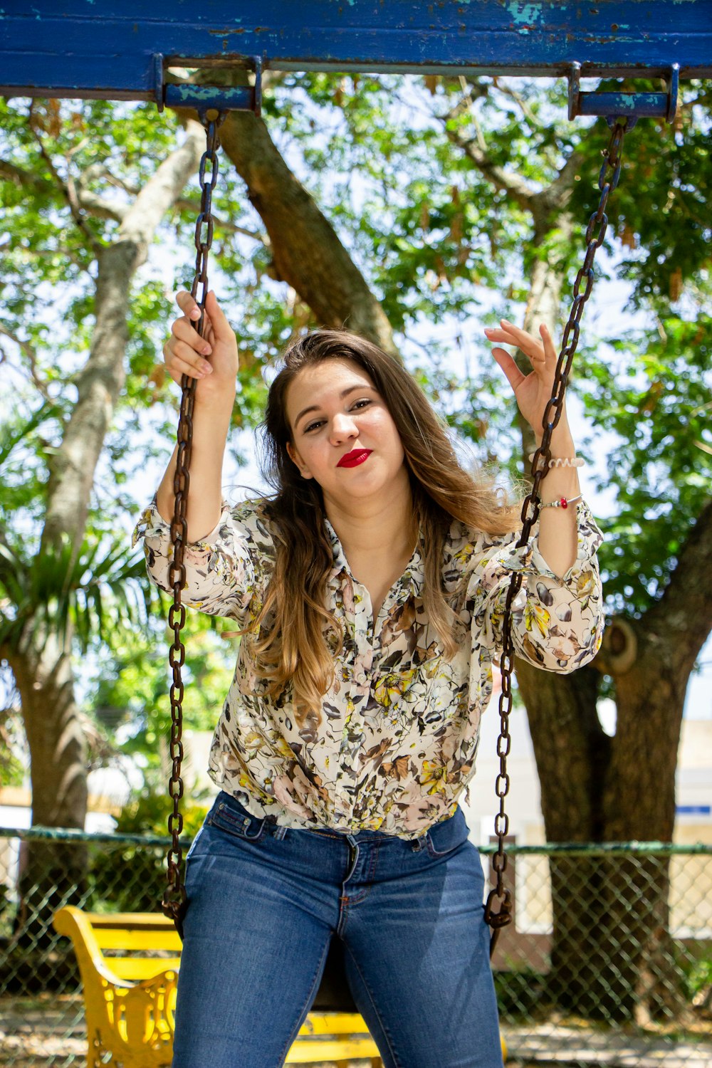 woman in brown and black floral shirt and blue denim shorts sitting on swing during daytime