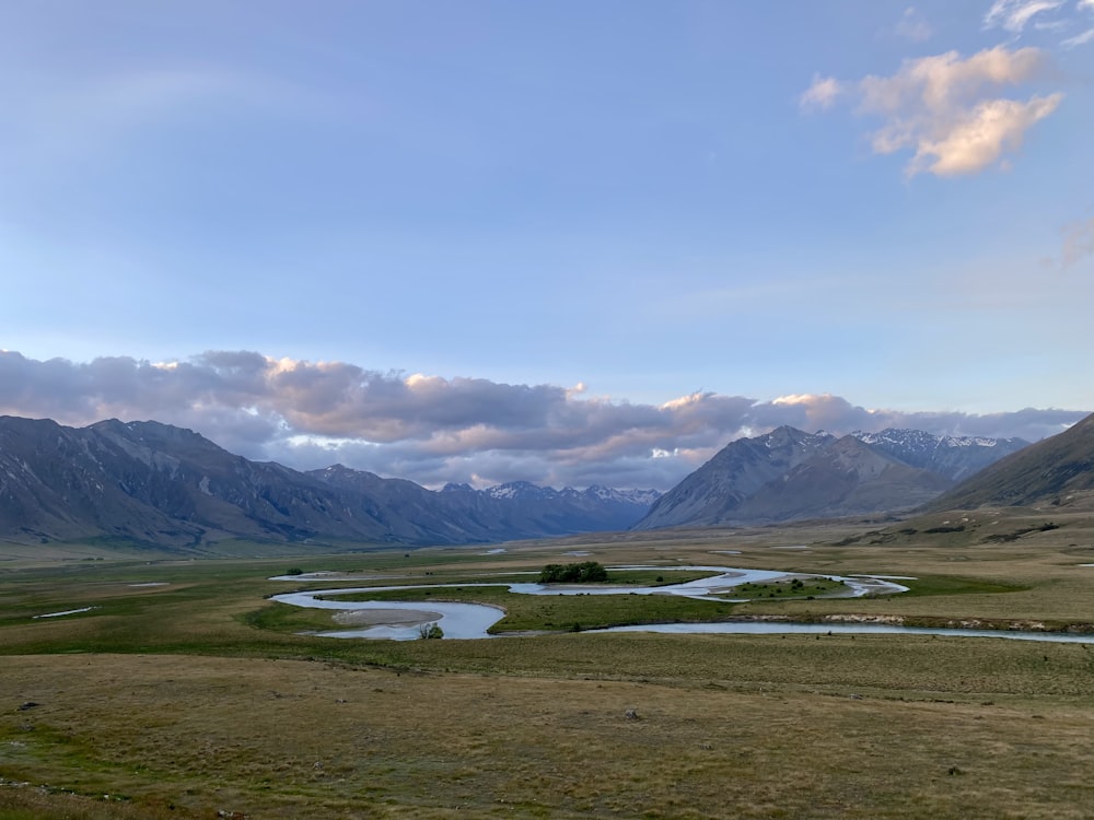 green grass field near mountain under white clouds during daytime