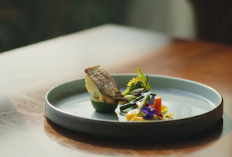 A sleek, modern seafood dish plated with fresh fish and garnishes in a minimalist blue and white setting.