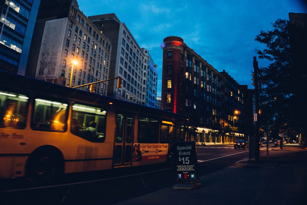 yellow bus on road near high rise buildings during night time