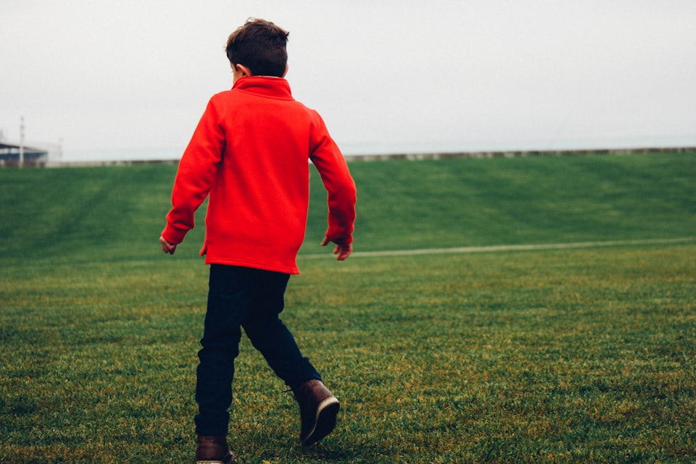 man in red hoodie standing on green grass field during daytime